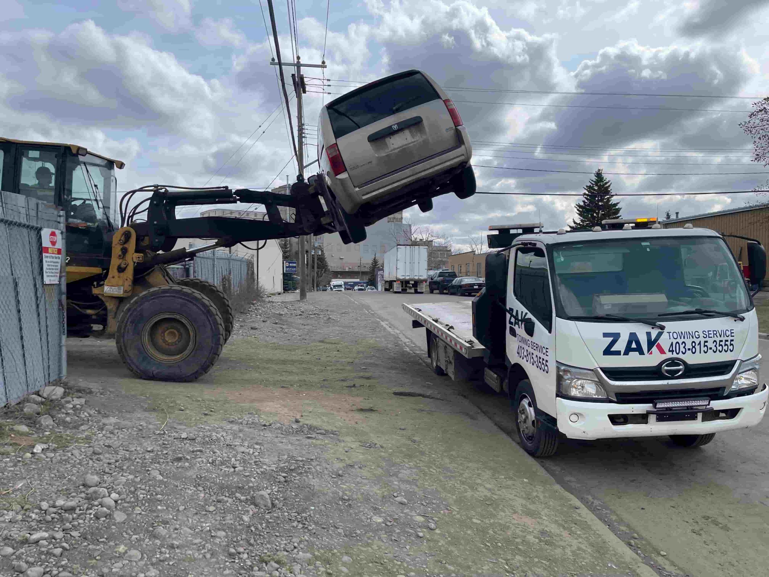 Loader lifting damaged van onto Zak Towing flatbed truck in Calgary