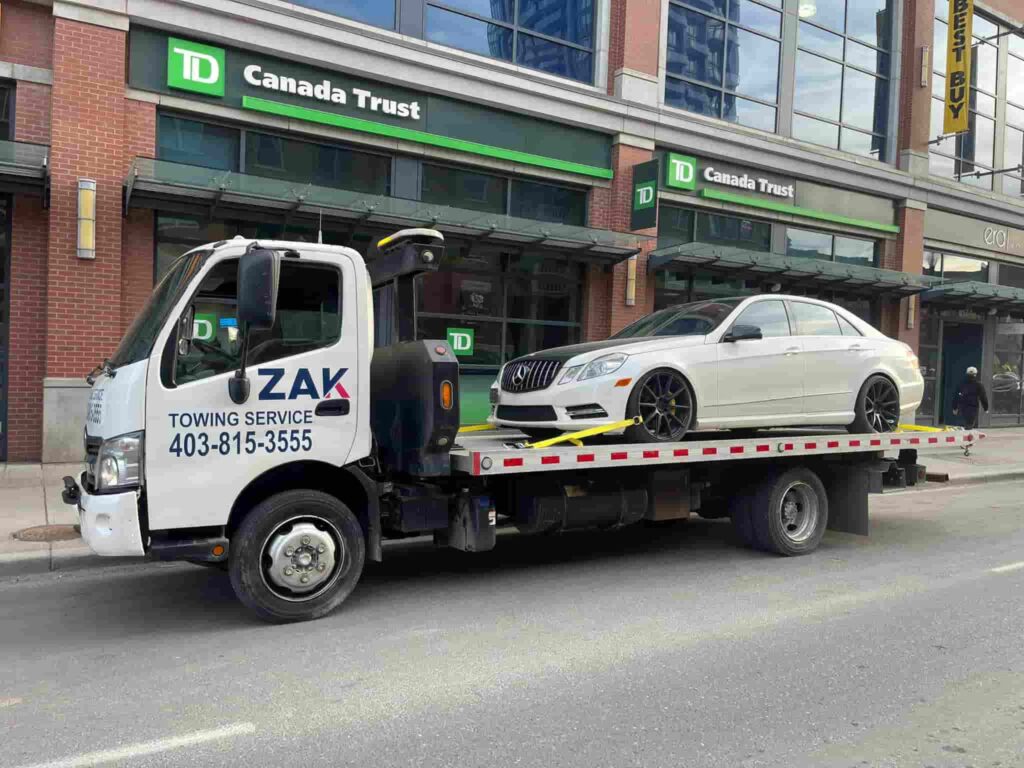 Zak Towing flatbed truck transporting a white luxury car in front of TD Canada Trust in downtown Calgary.