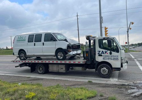 Zak Towing Service provides professional accident vehicle towing in Calgary, Alberta. A damaged GMC van is safely loaded on a flatbed tow truck at a city intersection. Our emergency towing service ens...Sorry but this string is too long !!!