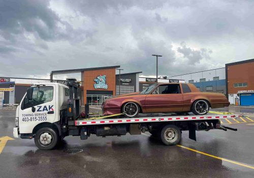 Zak Towing Service safely transports a classic car on a flatbed tow truck in Calgary, Alberta. Professional vehicle towing performed in a commercial area under cloudy weather conditions. We provide re...Sorry but this string is too long !!!