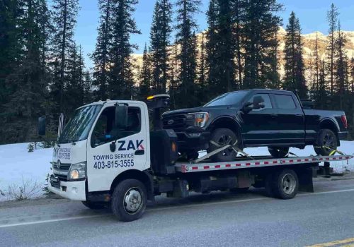 Loader lifting damaged van onto Zak Towing flatbed truck in Calgary