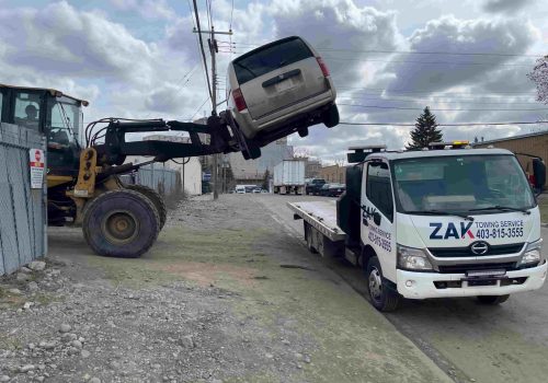 Loader lifting damaged van onto Zak Towing flatbed truck in Calgary